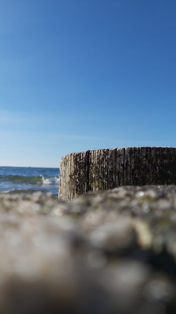 Einzelner Buhnenpfahl vor ruhigem Himmel und Meer – steht für Minimalismus und Reduktion in der Bildgestaltung