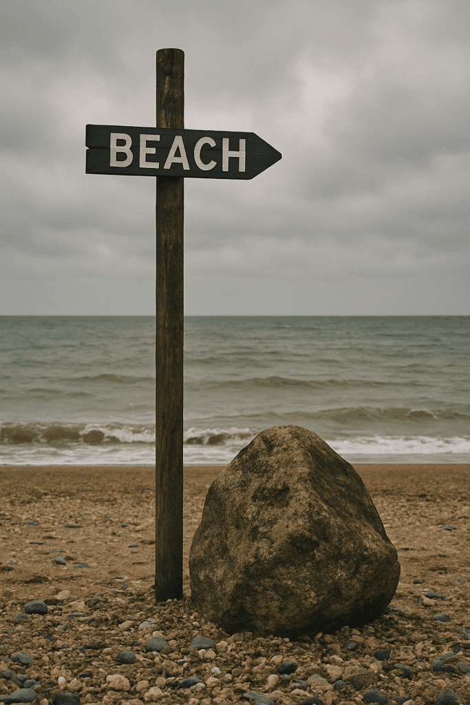 Ein Schild mit der Aufschrift „BEACH“ steht mittig vor einem felsigen Strand, während ein großer Stein im Vordergrund die Bildwirkung dominiert – Beispiel für falsche Motivplatzierung nach der Drittelregel