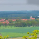 Luminar Neo Anfänger Workflow: Blick über grüne Felder auf ein Dorf mit rotem Kirchendach und Kirchturm unter grauem Himmel