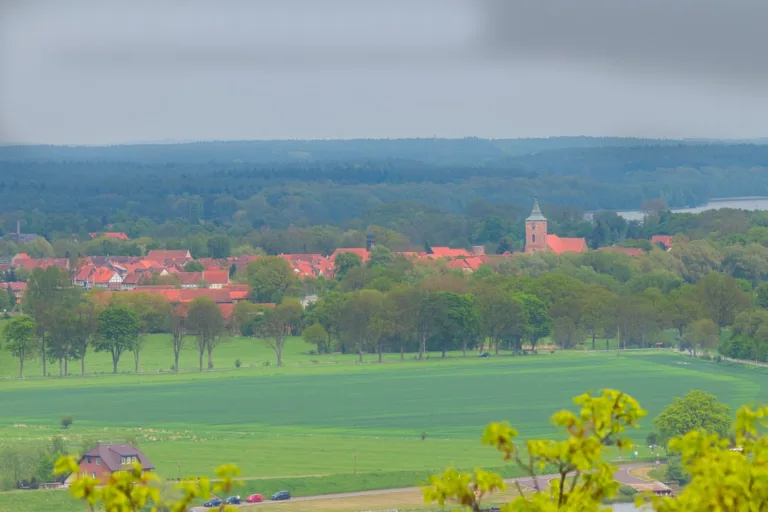 Luminar Neo Anfänger Workflow: Blick über grüne Felder auf ein Dorf mit rotem Kirchendach und Kirchturm unter grauem Himmel